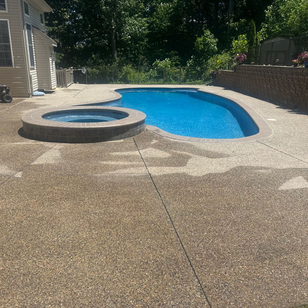 Backyard pool with attached hot tub and tan concrete deck in bright sunlight