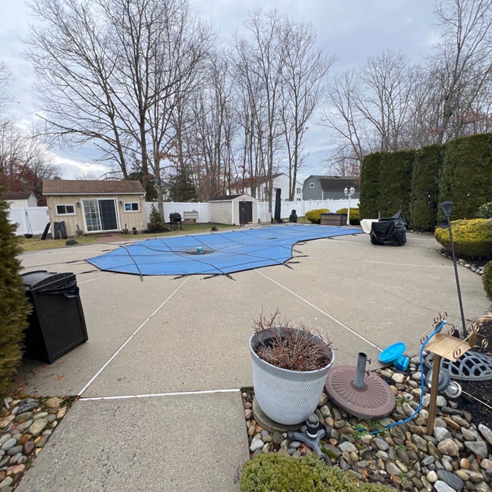 Backyard patio with a blue tarp covering the center, potted plant, rocks, and trimmed hedges under bare trees