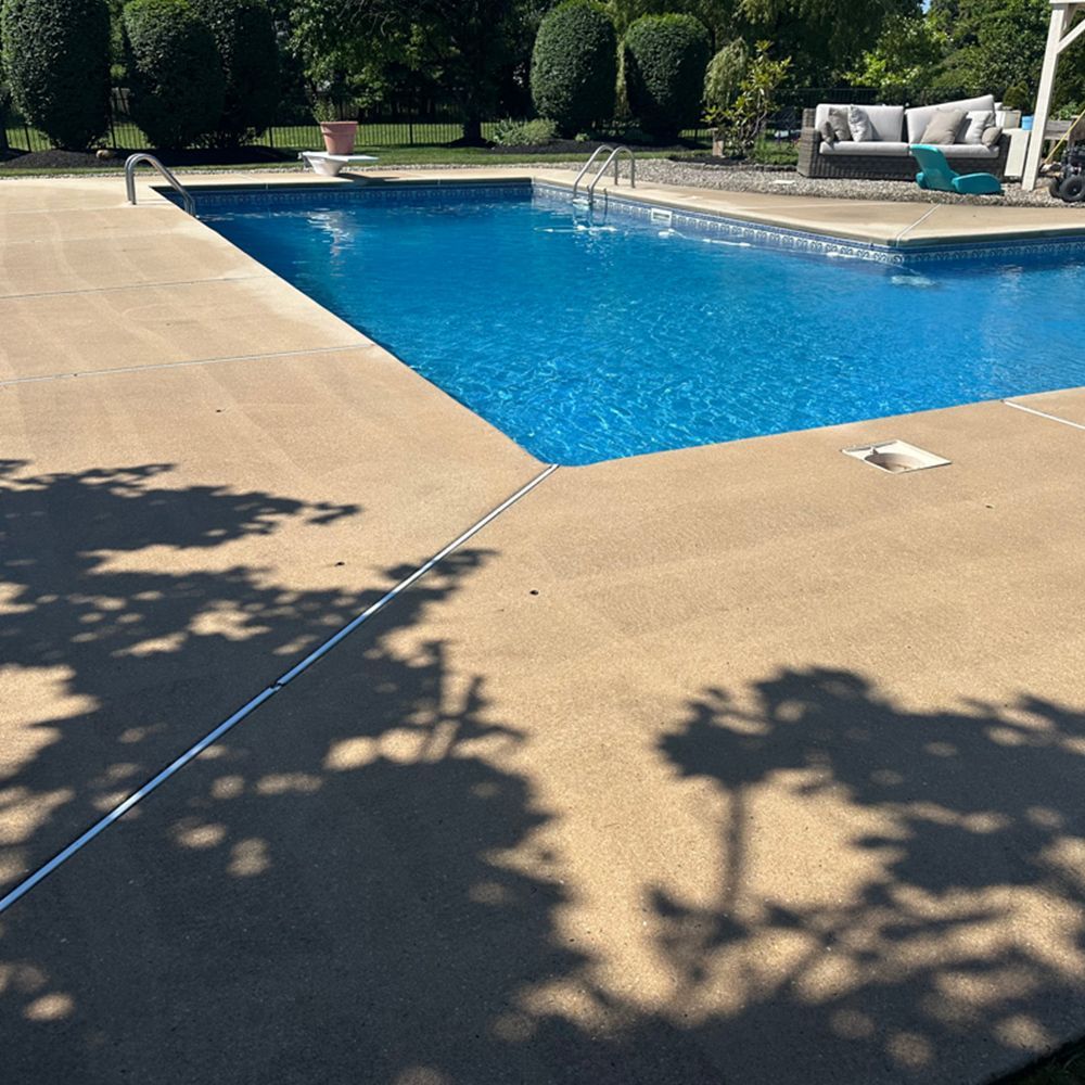 Backyard swimming pool with tan deck, blue water, and shaded lounge chairs.