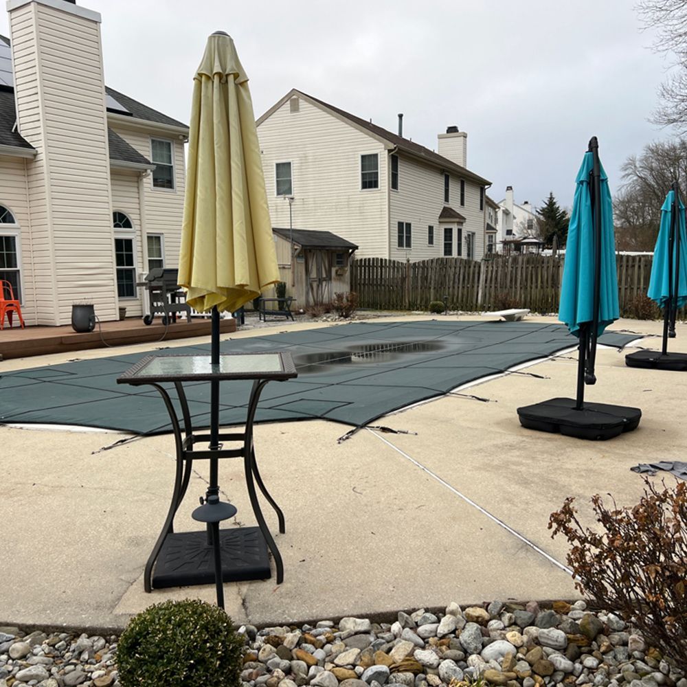 Patio with closed umbrellas and tables beside a covered pool in a suburban apartment courtyard