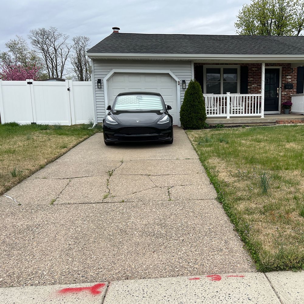 Black car parked in a driveway of a suburban house with a white fence and porch