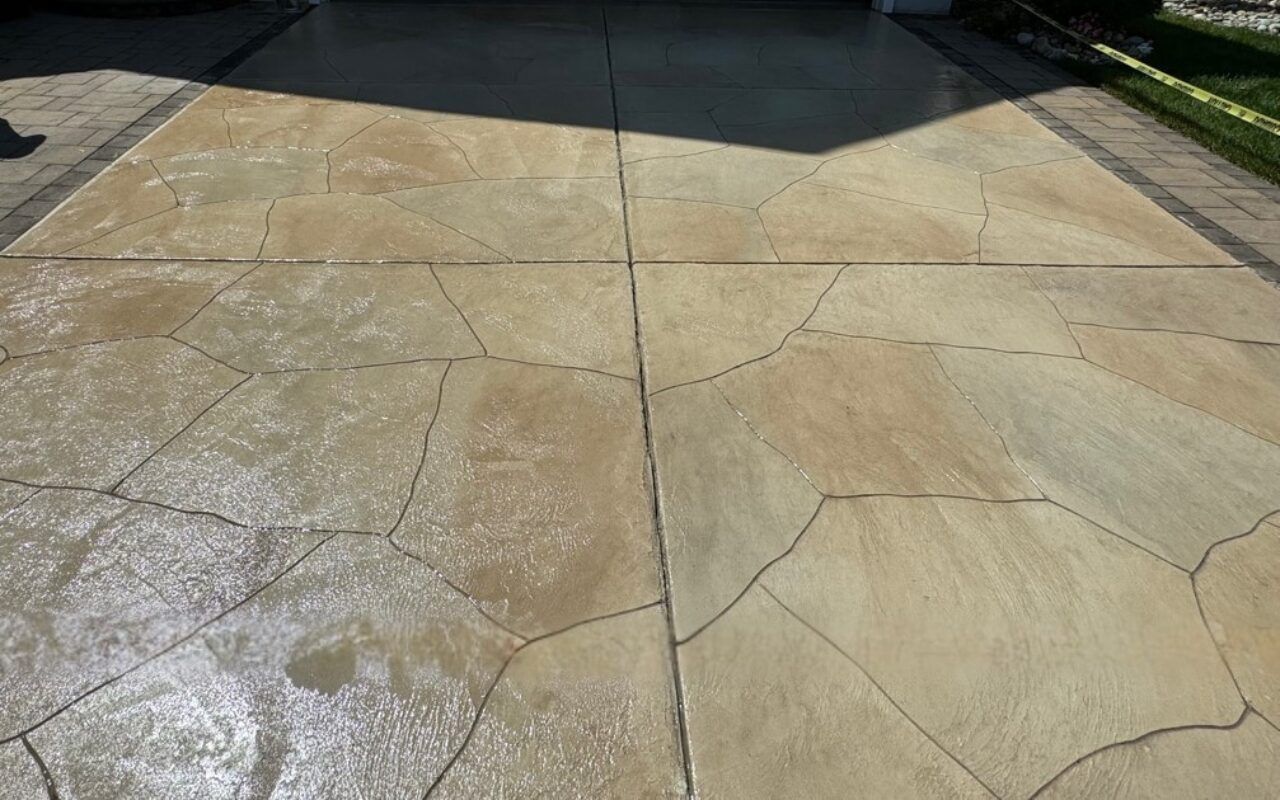Cracked beige concrete driveway leading to a dark garage or shaded area.