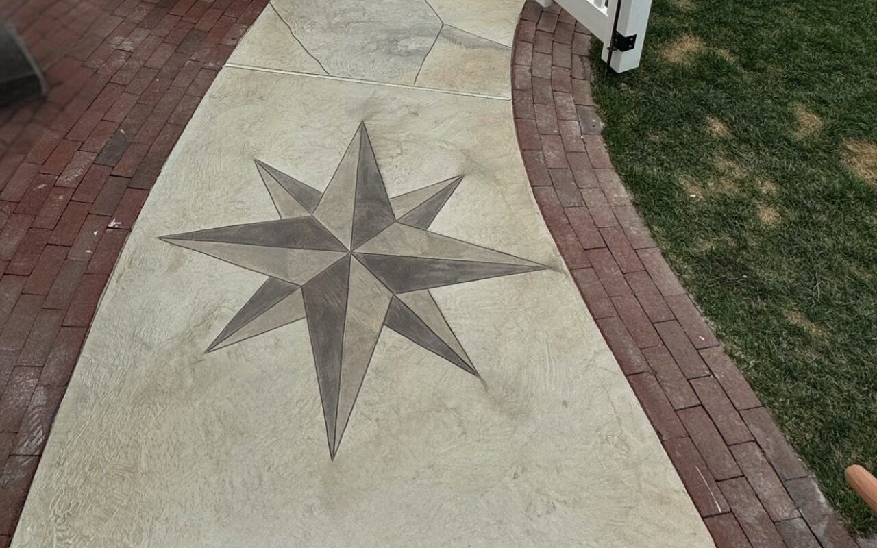 Concrete sidewalk with a dark star mosaic beside brick edging and grass