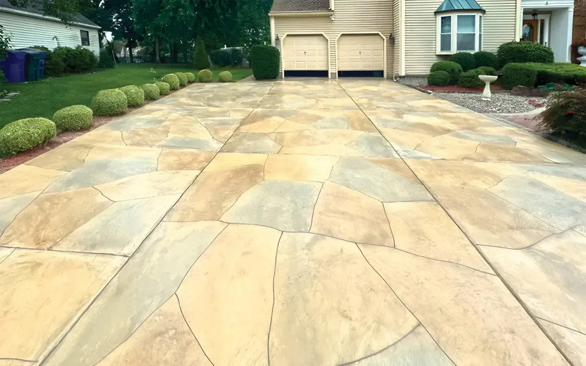 Stone driveway leading to a beige house with a garage, bordered by green shrubs