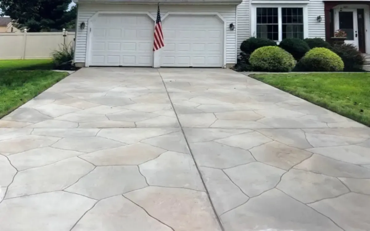 Wide concrete driveway leading to a white house with a garage and an American flag