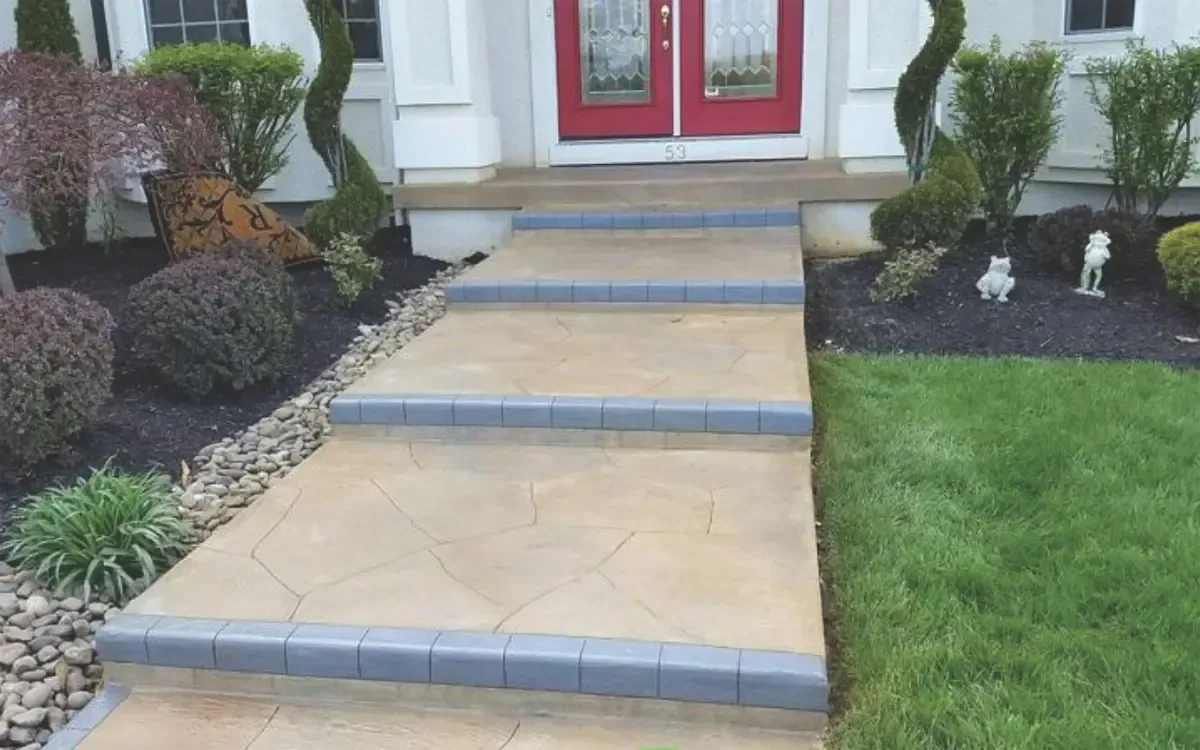 Front walkway with tan steps and blue edging leading to red double doors, flanked by shrubs and lawn