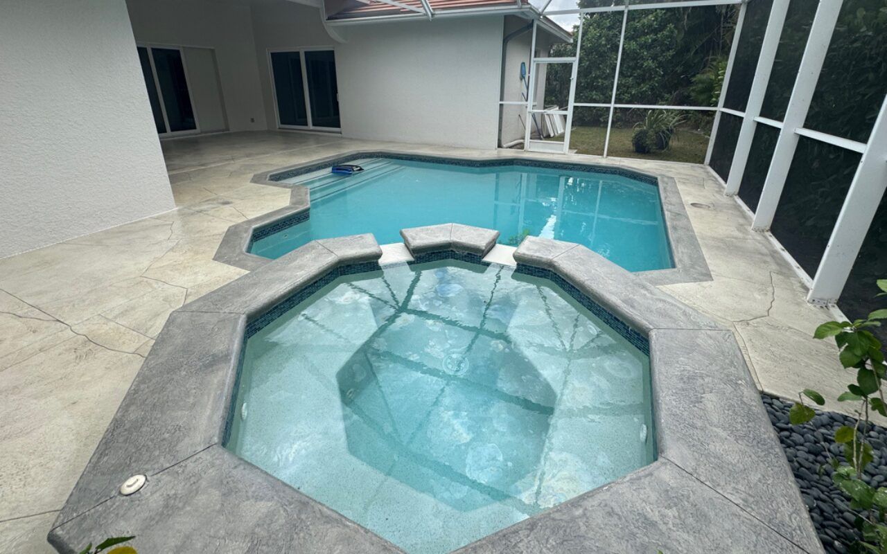 Patio with a small hexagonal spa beside a blue swimming pool, surrounded by a screened enclosure