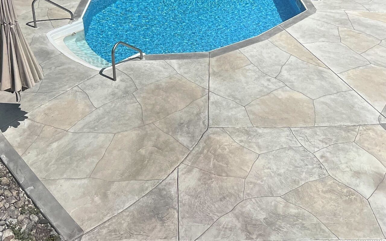 Stone patio beside a blue swimming pool with a metal handrail and patio umbrella base