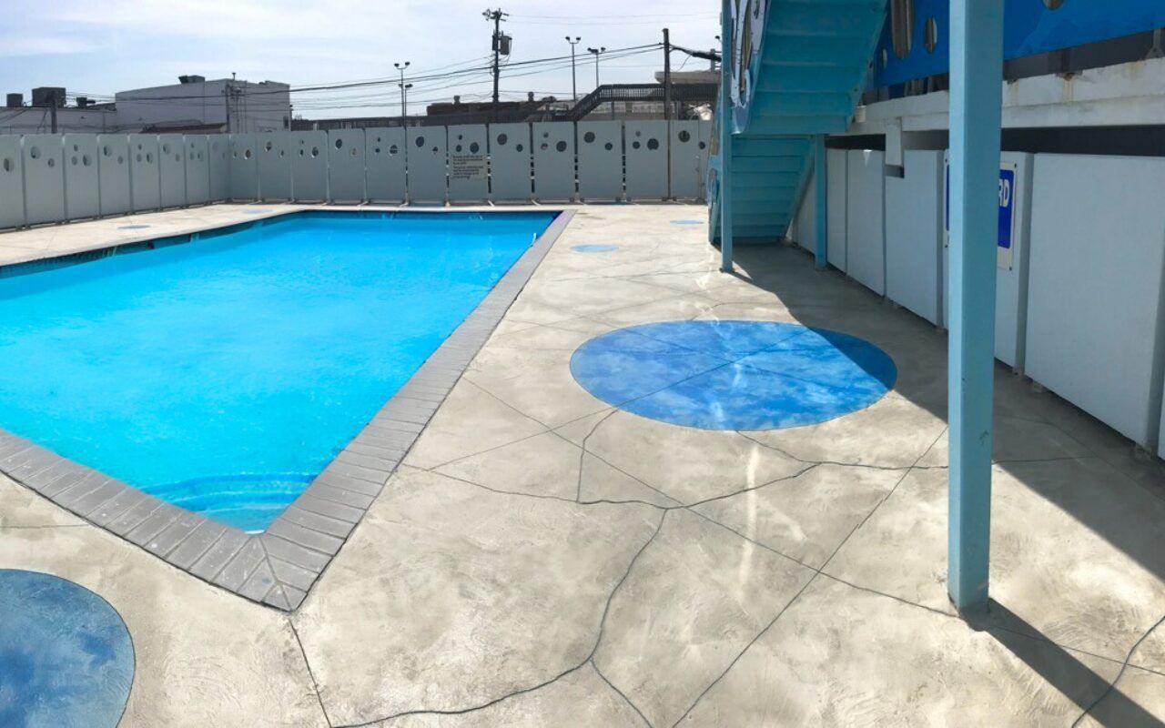 Rooftop pool with bright blue water, concrete deck, and blue shade structure under a clear sky