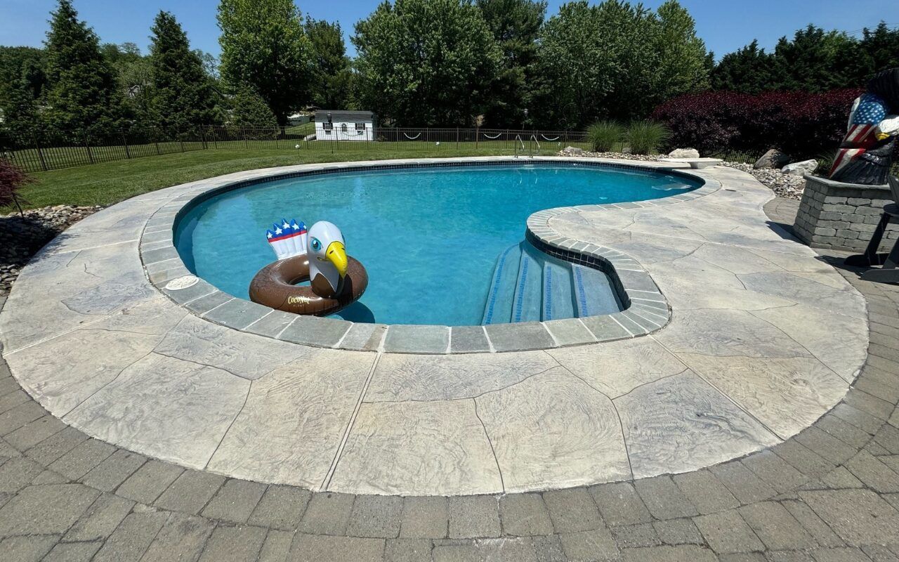 Backyard swimming pool with stone patio and a colorful float near the steps