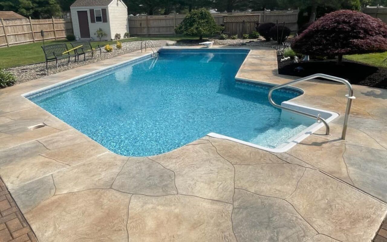Backyard swimming pool with blue water, stone patio, steps, and a small white shed in the background