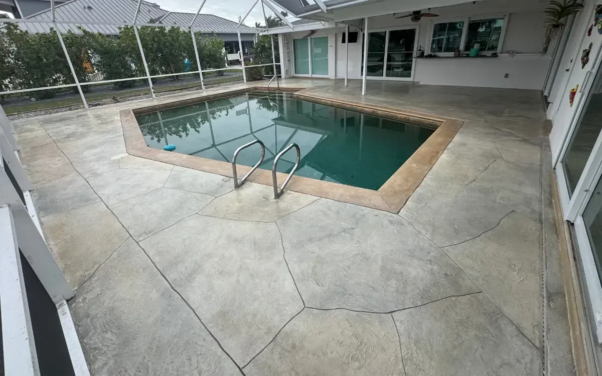 Backyard pool with light stone patio and metal handrail under a covered patio area