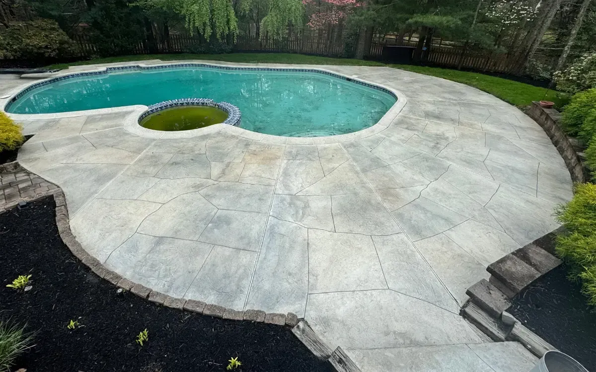 Backyard pool with turquoise water and a large curved concrete deck surrounded by trees