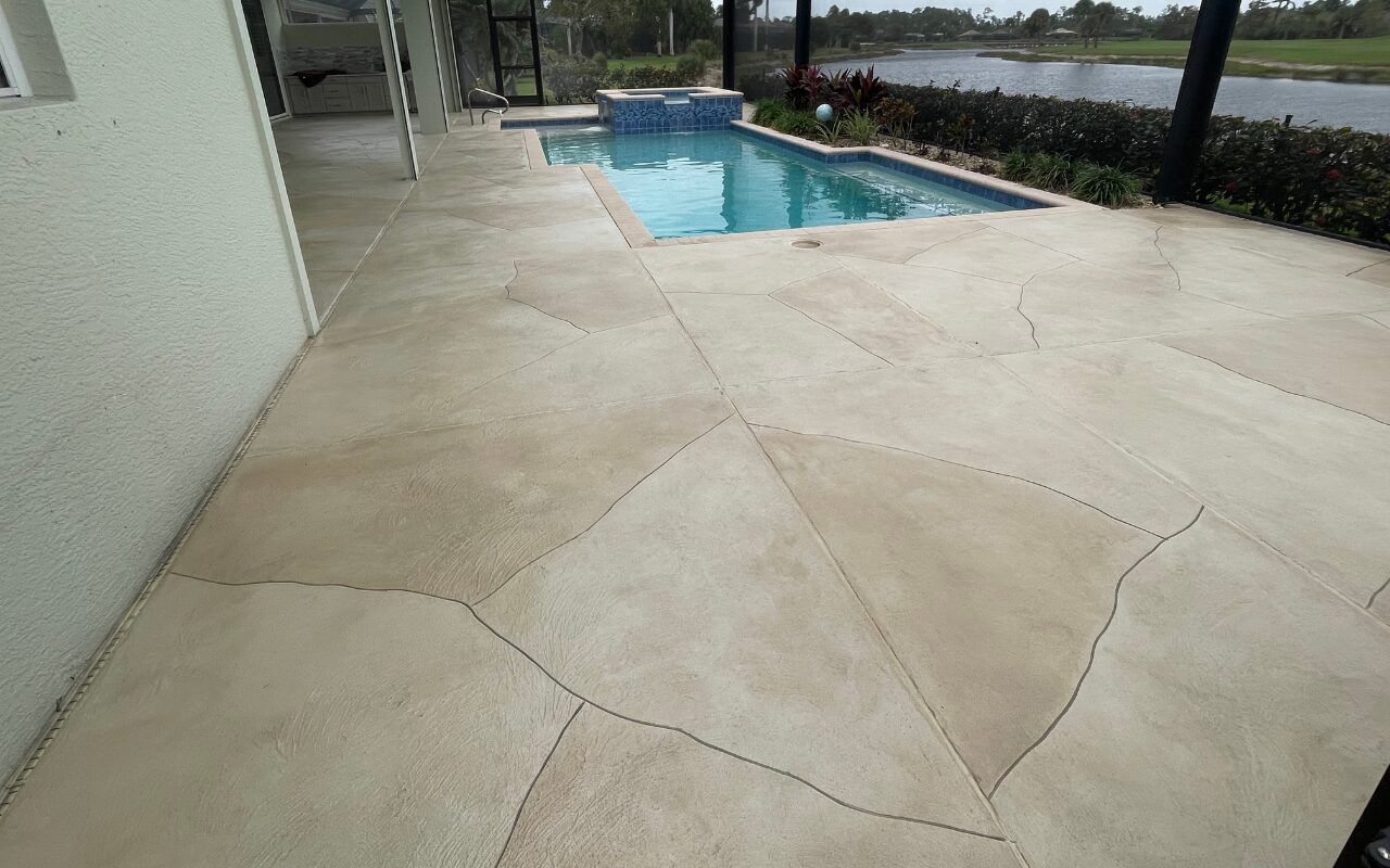 Concrete patio beside a backyard pool and screened enclosure, with water and trees in the distance.