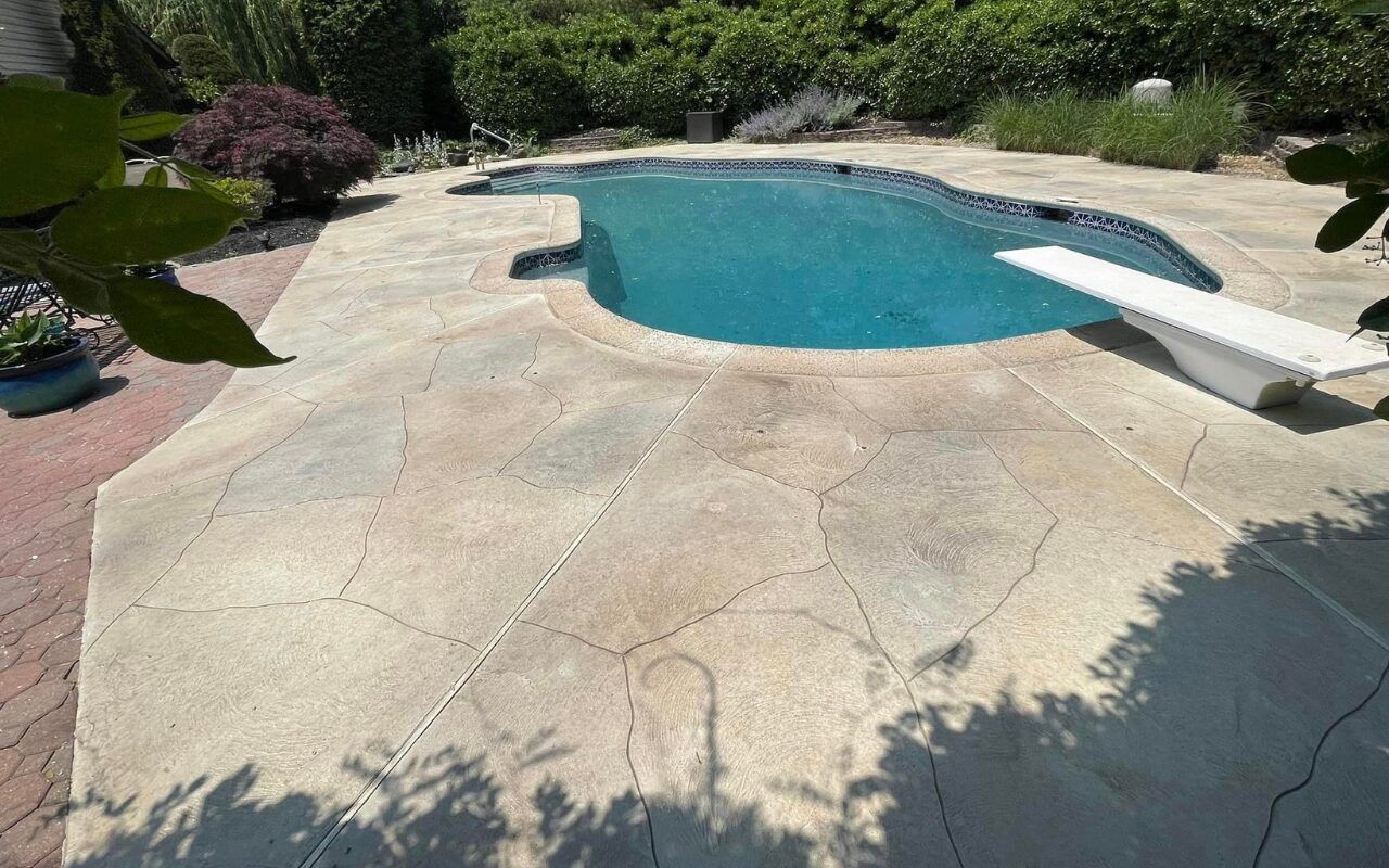 Backyard swimming pool with tan concrete patio, slide, and surrounding greenery
