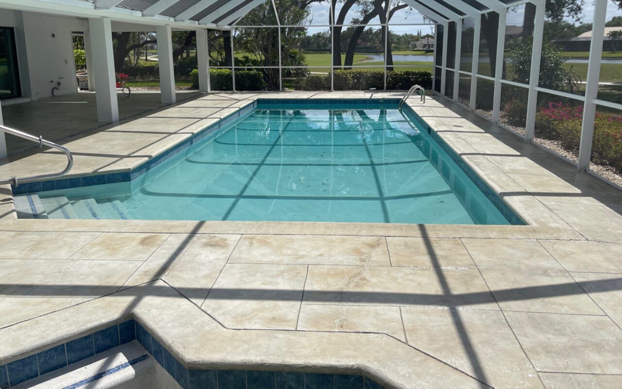 Covered indoor pool with turquoise water, tiled deck, and screened enclosure with sunlight streaming in.