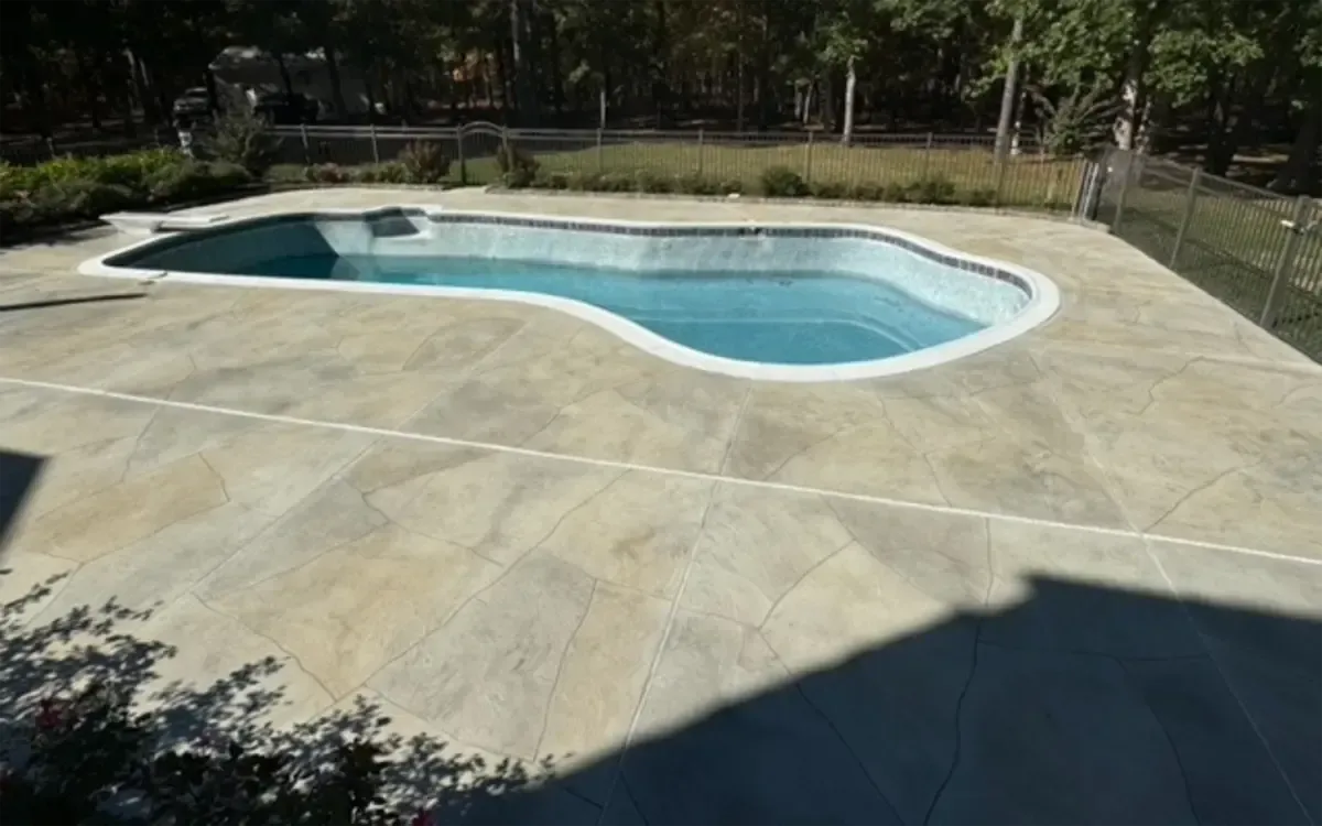 Empty backyard swimming pool and large concrete deck surrounded by trees and a chain-link fence