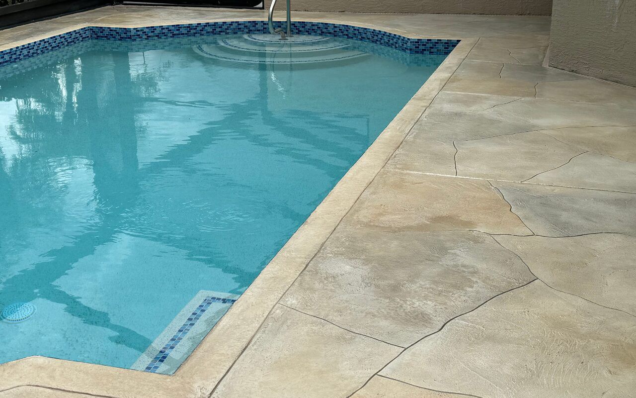 Backyard swimming pool with clear blue water beside a tan stone patio
