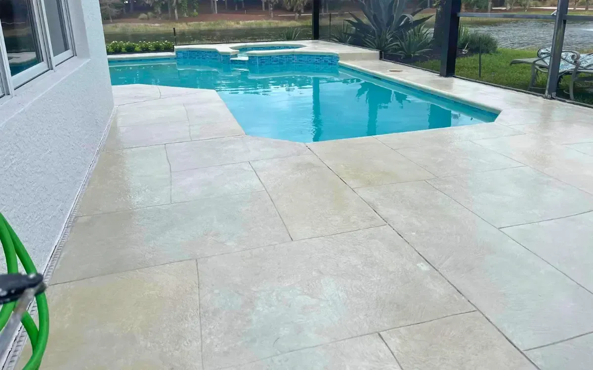 Backyard swimming pool beside a light stone patio and white house wall