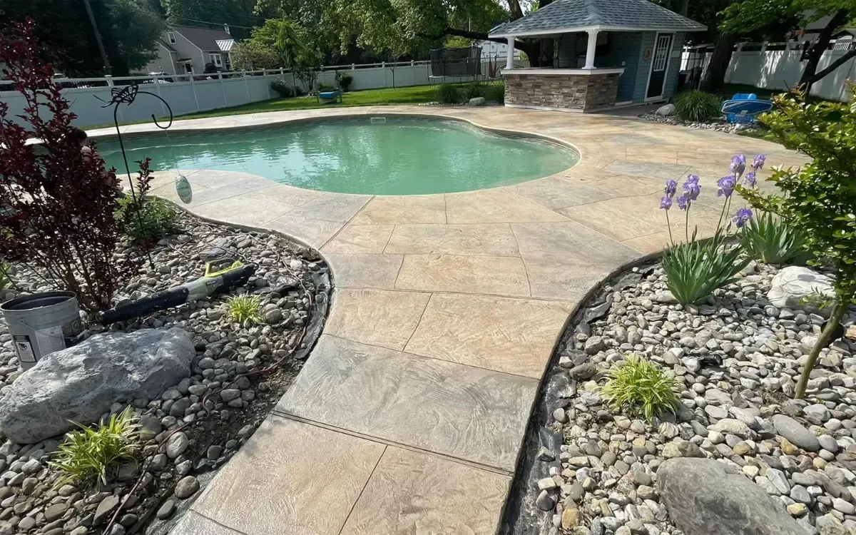 Backyard pool with curved stone patio, landscaped rock beds, and a gazebo by the water