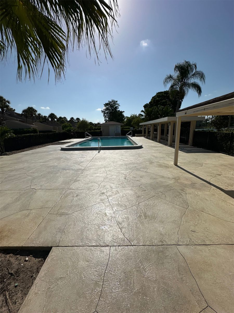 Sunlit patio with a central swimming pool, palm trees, and a covered seating area under a clear blue sky