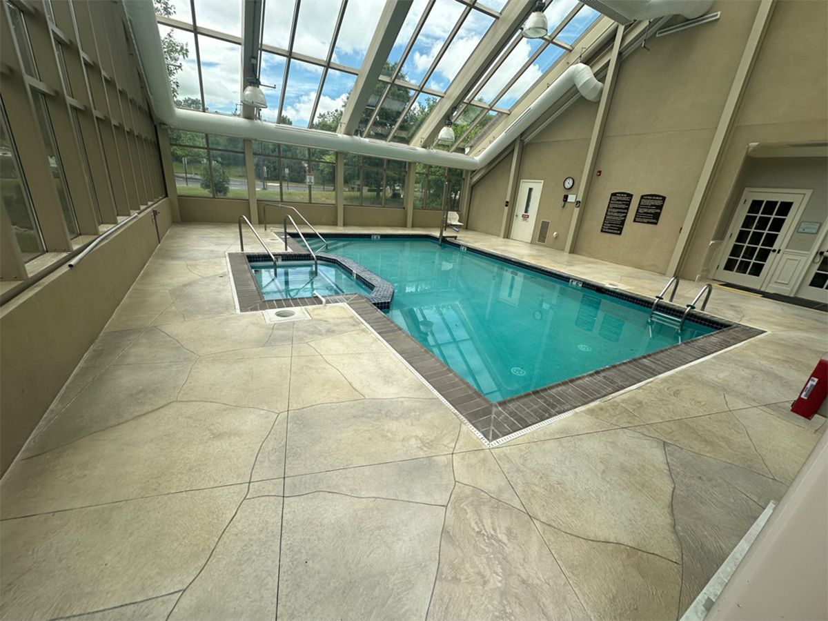 Indoor pool with turquoise water, glass ceiling, and beige tiled deck