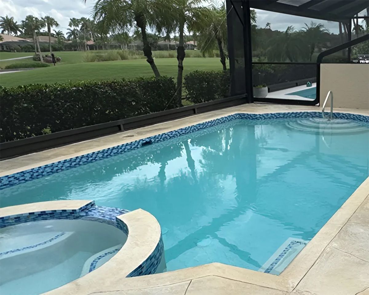Backyard swimming pool with a spa, screened enclosure, and palm trees beyond the hedge