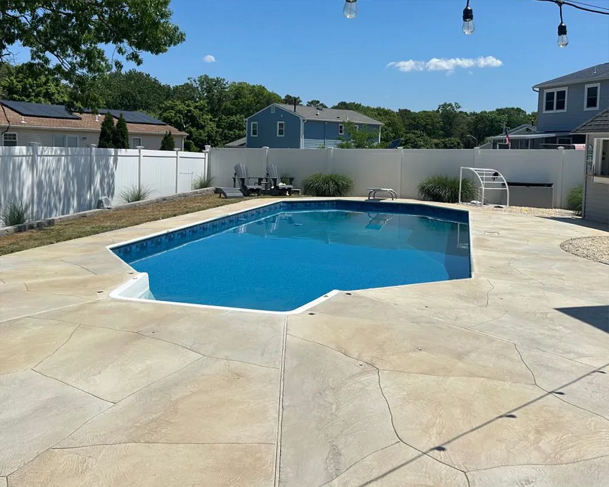 Backyard swimming pool with a stone deck and white fence on a sunny day