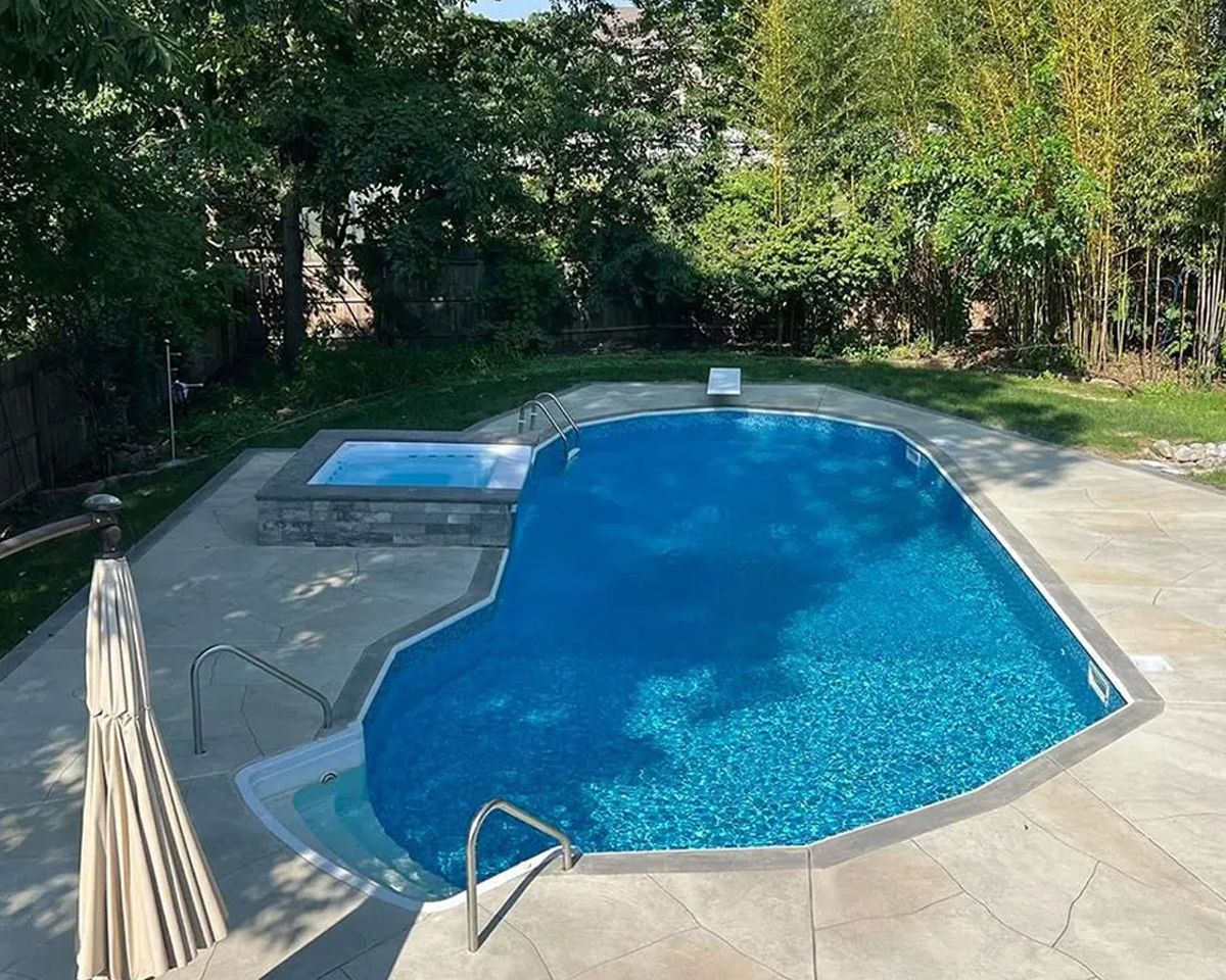Backyard swimming pool with a hot tub, stone deck, and surrounding trees