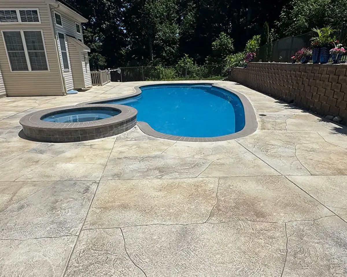 Backyard swimming pool with attached hot tub beside a patio and stone wall