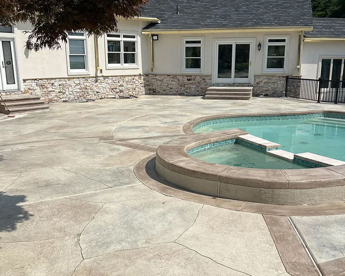Backyard patio with a swimming pool, stone deck, and house exterior.
