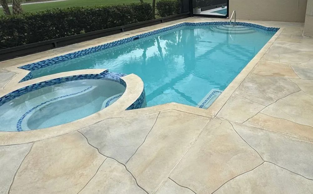 Backyard swimming pool with attached spa and beige stone patio beside hedges