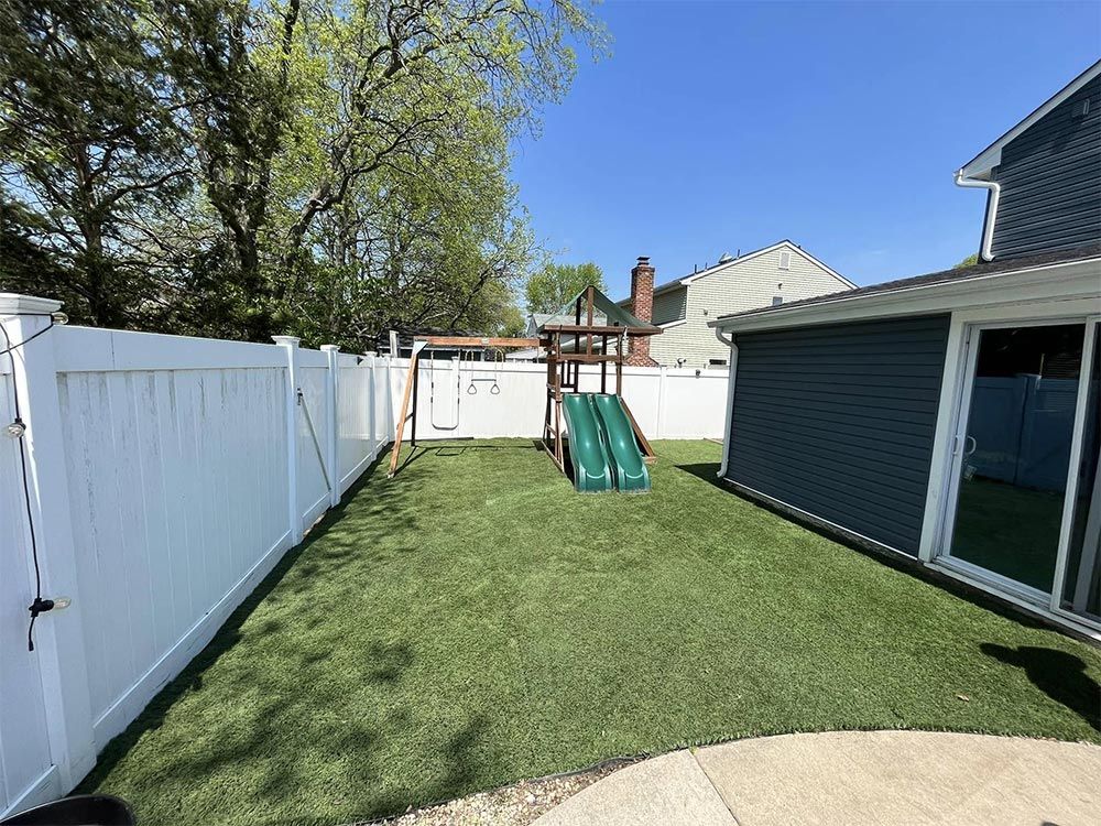 A backyard with a playground and a white fence.