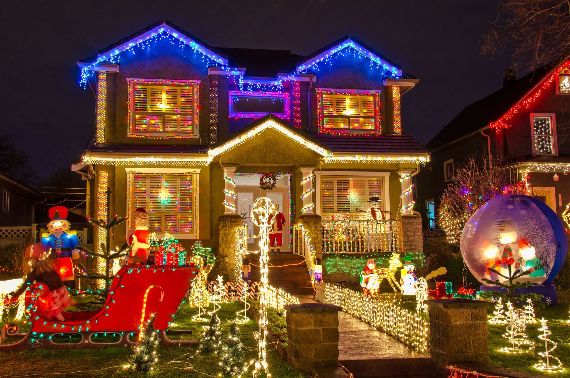 House decorated with bright Christmas lights, including a sleigh and a large snow globe ornament.