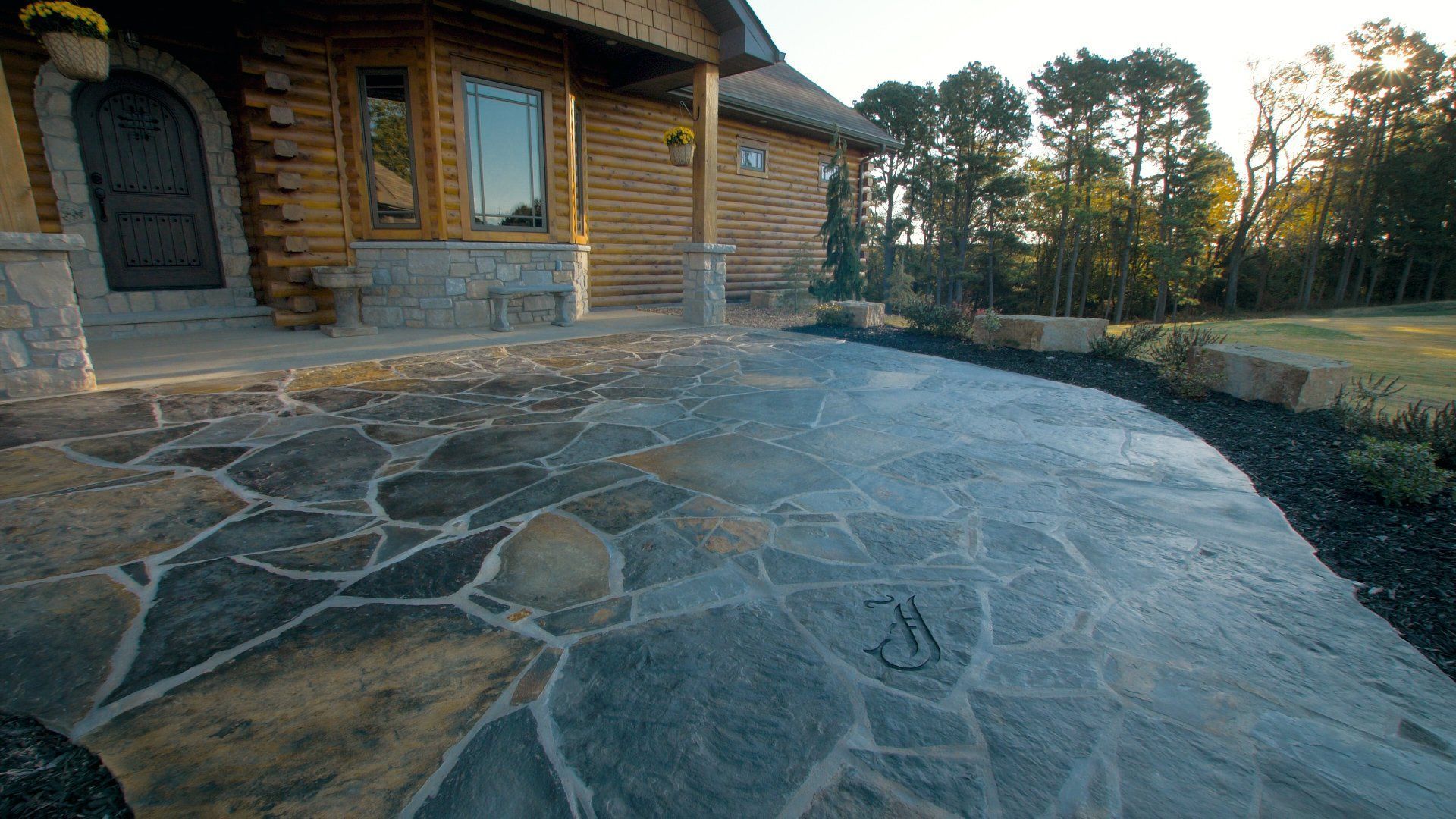 Stone patio leading to a wooden house with a curved path and landscaping.