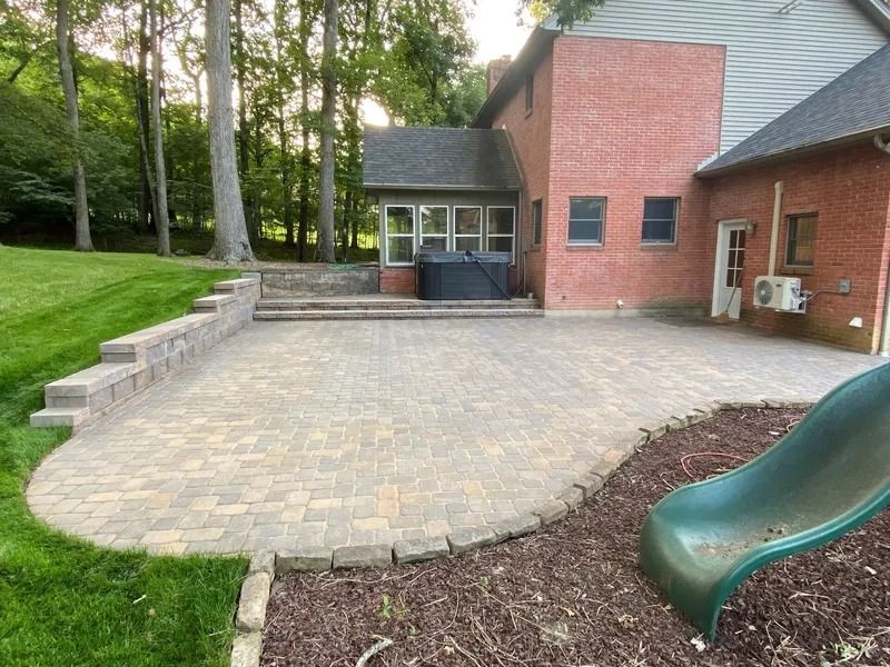 Brick patio with retaining wall, lawn, and brick house. A green slide is in the foreground.