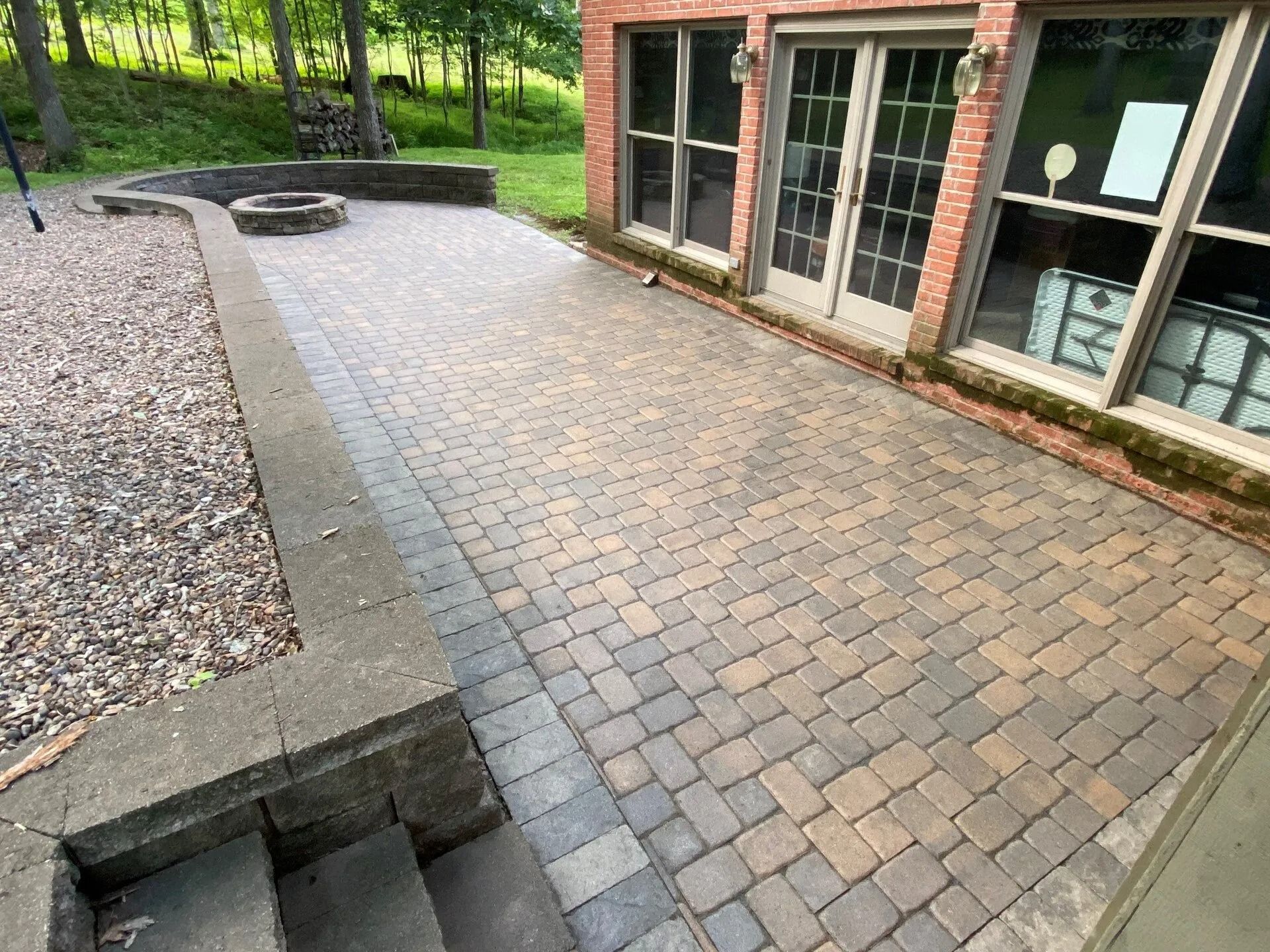 Brick patio with fire pit and steps, adjacent to a brick building with windows.