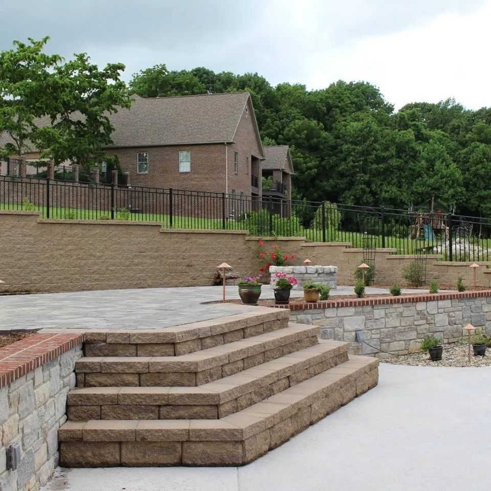 Stone steps lead to patio, retaining walls with plants, house in the background.