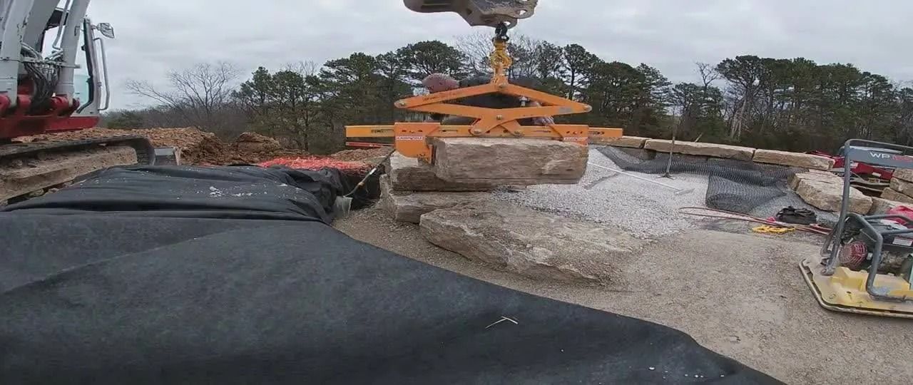 A large machine lifting a large stone block at a construction site.