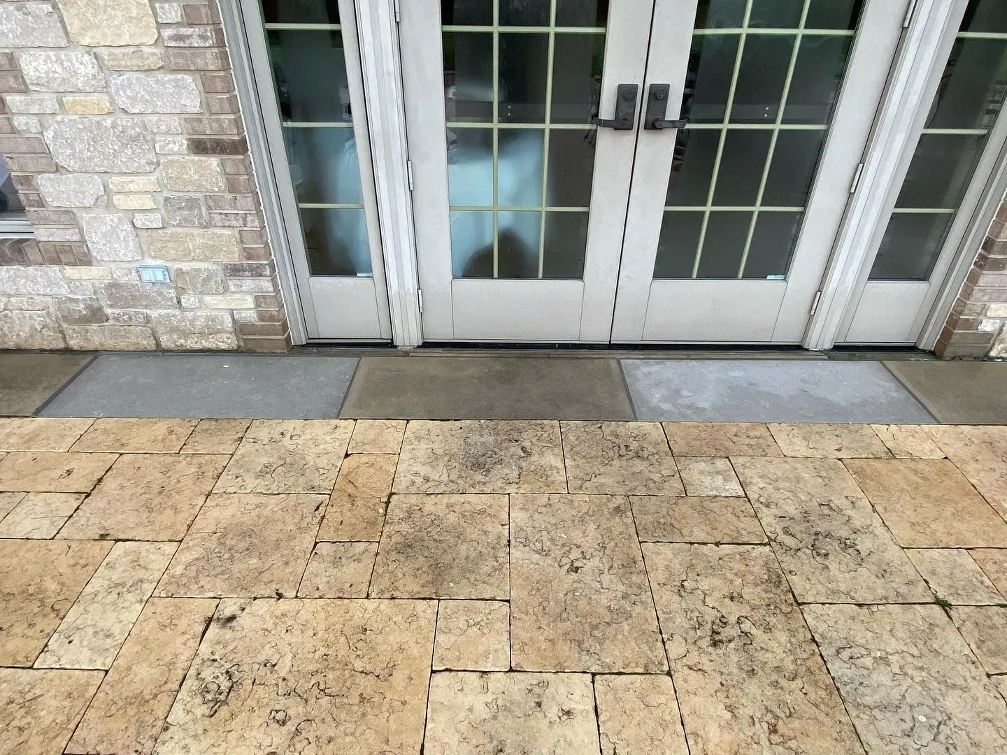 Stone patio leading to white French doors with brick siding.