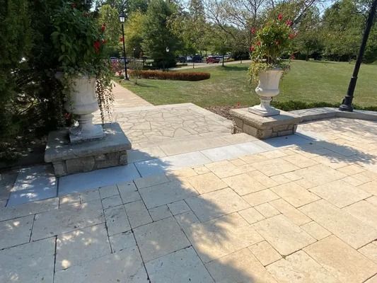 Stone patio with steps, urns of flowers, and a grassy park in the background.