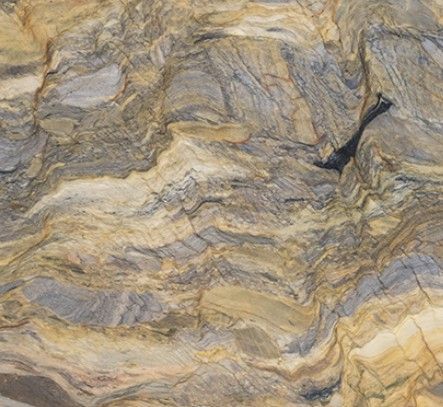 A close-up of natural stone with swirling, organic patterns in shades of tan, brown, grey, and deep blue-black.