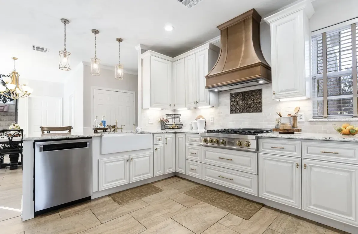 White kitchen with stainless steel appliances, copper hood, and beige tile floor.