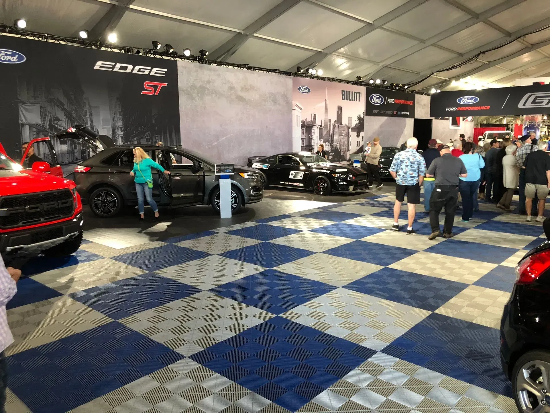 Ford car display tent with vehicles on checkered floor; people viewing.