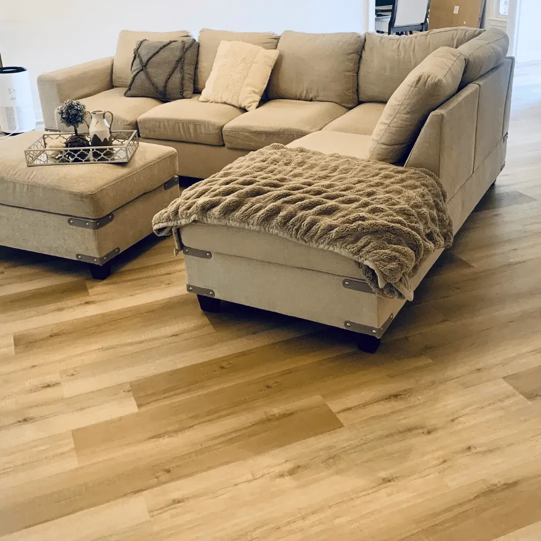 Beige sectional sofa and ottoman with throw blanket, on light wood-look flooring.