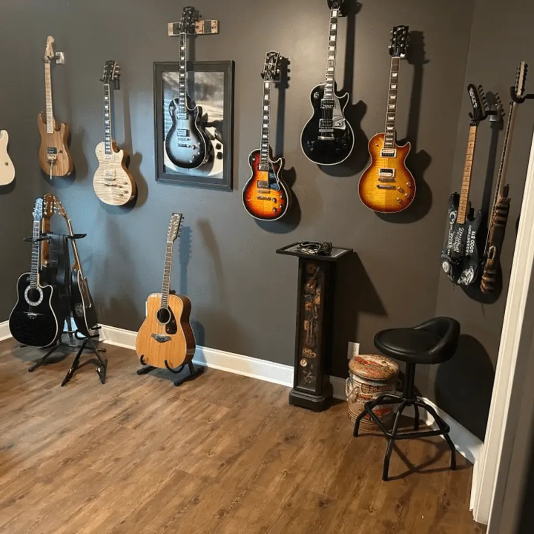 A room with guitars hanging on the wall and on stands; a stool and a stand-alone ash tray.