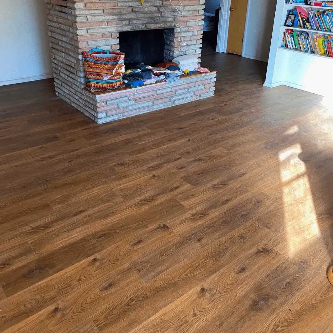Hardwood-like flooring in a room with a brick fireplace and shelves with colorful items.