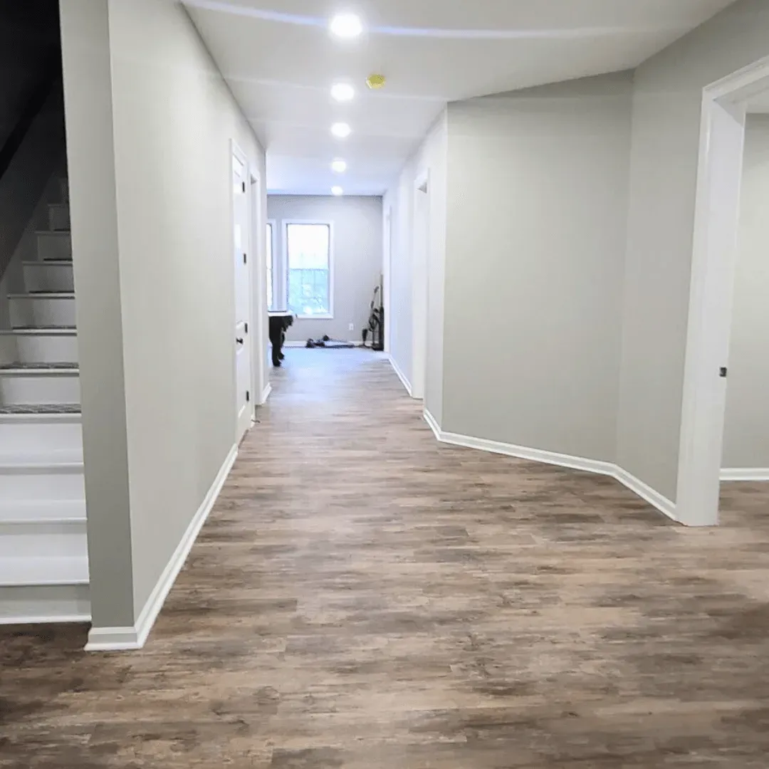 Hallway with wooden floor, white trim, and gray walls, leading to a window.