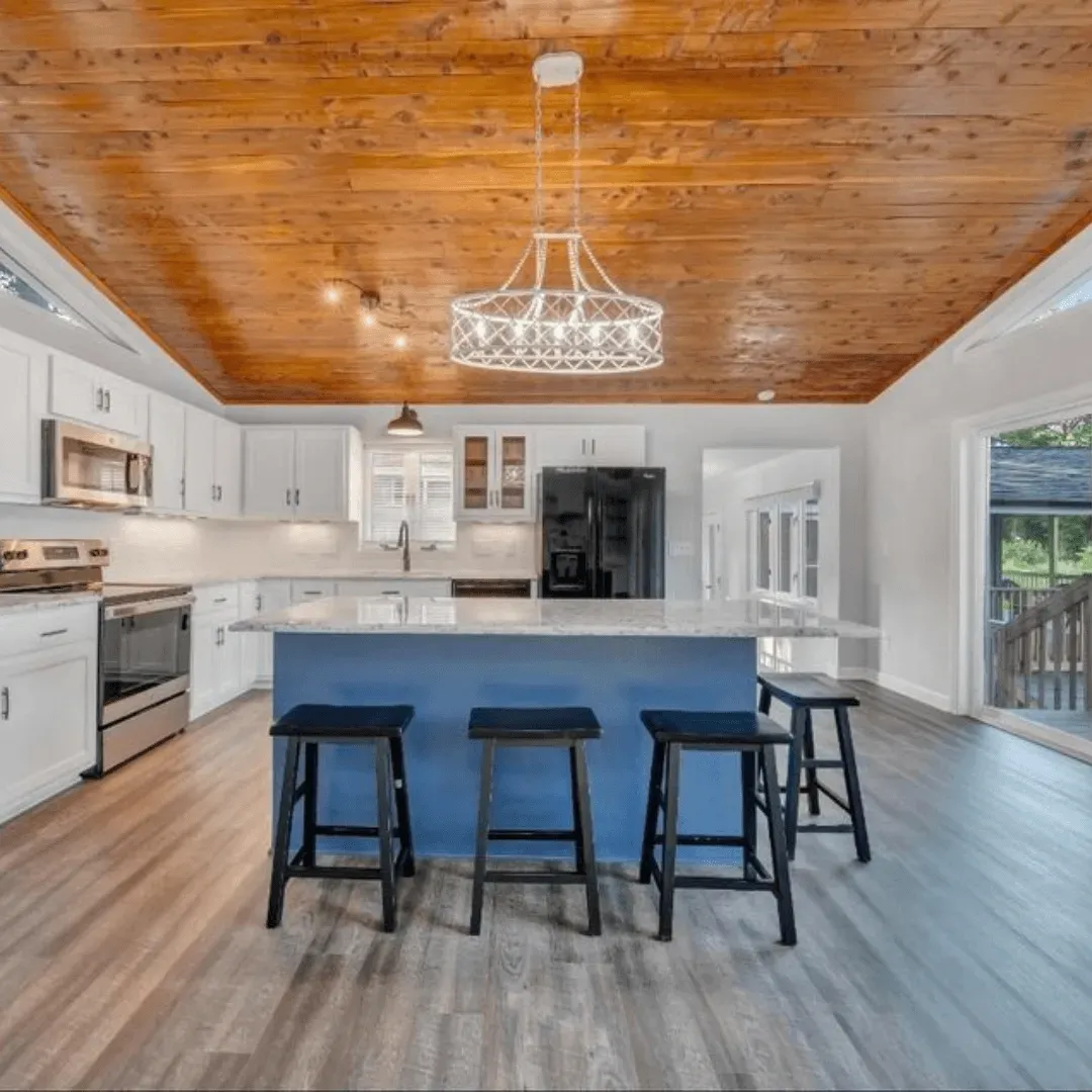 Kitchen with wood ceiling, blue island with stools, white cabinets, stainless appliances, and a chandelier.