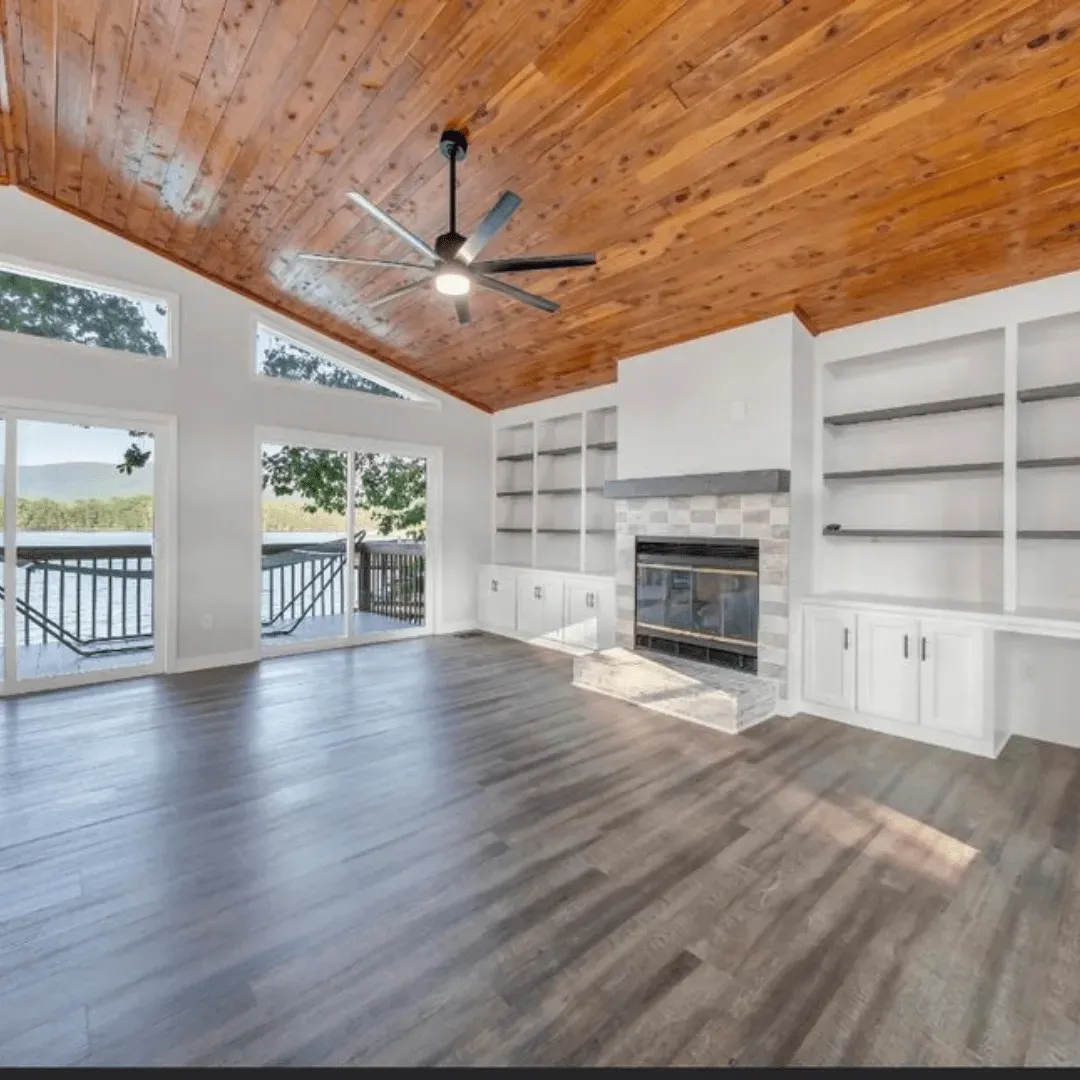 Spacious living room with wood ceiling, dark wood floors, white built-ins, and a fireplace. Sliding doors lead to a deck.